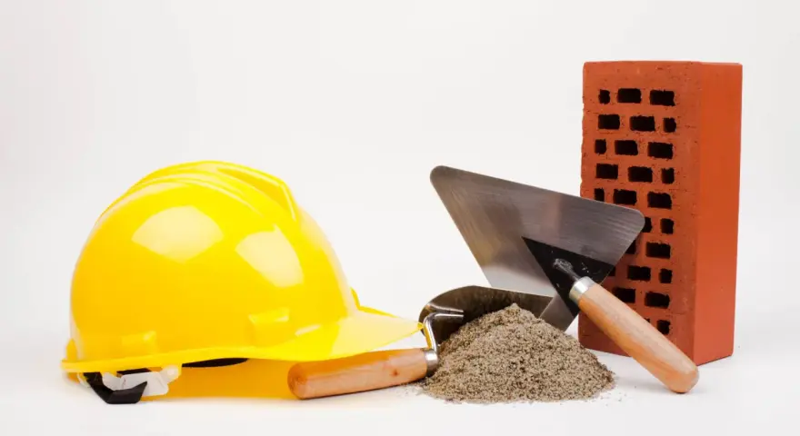 Casque jaune, brique rouge, tas de sable et truelles : les outils maçon essentiels pour bâtir.