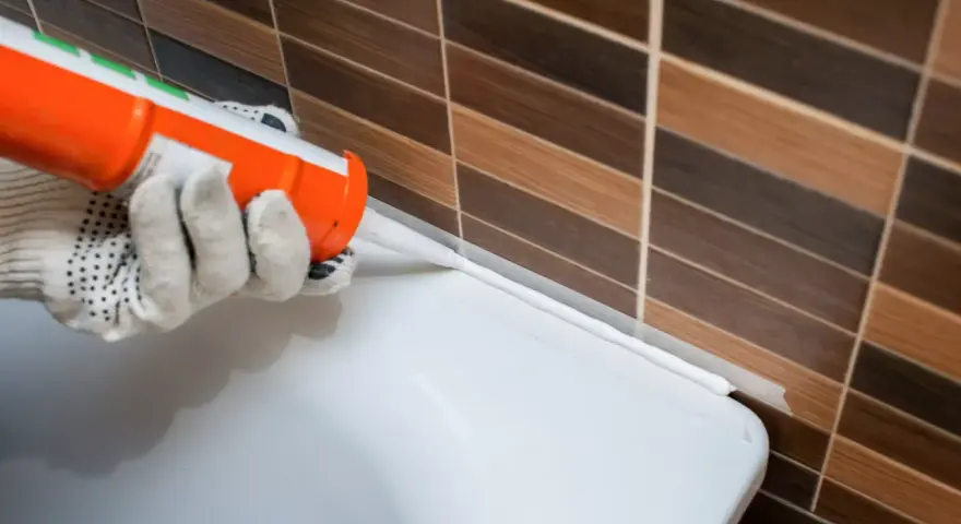 Application d'un joint acrylique ou silicone blanc pour étanchéifier le bord d'une baignoire contre un mur carrelé.