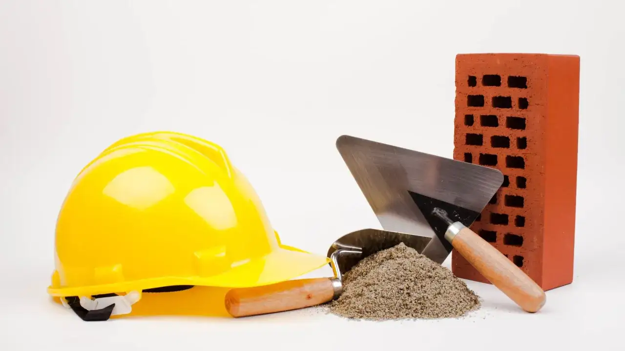 Casque jaune, brique rouge, tas de sable et truelles : les outils ma&ccedil;on essentiels pour b&acirc;tir.