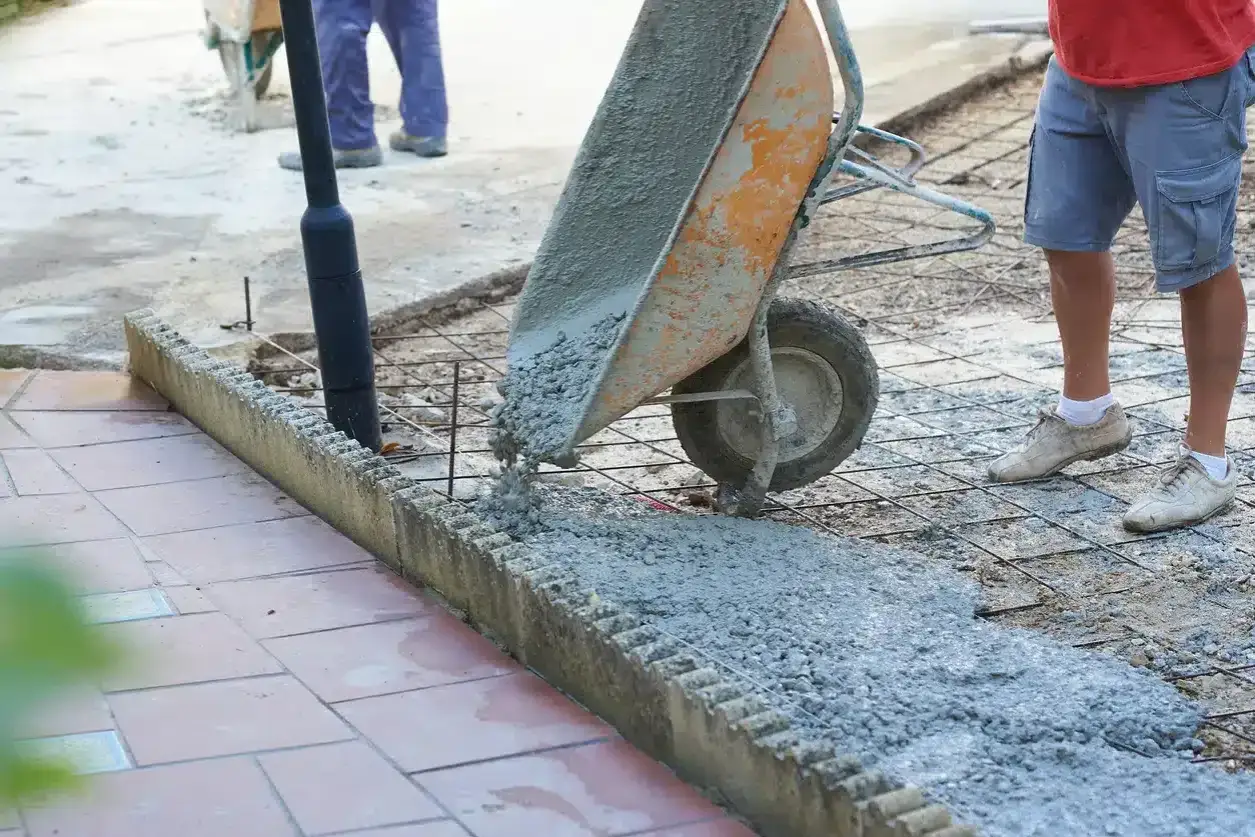 Brouette d&eacute;versant du b&eacute;ton frais sur une armature m&eacute;tallique. Mat&eacute;riaux pour terrasse b&eacute;ton en cours d'installation.