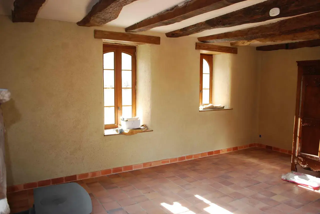 Murs en chaux chanvre pour une isolation naturelle. La lumière traverse les fenêtres, illuminant le sol en terre cuite.