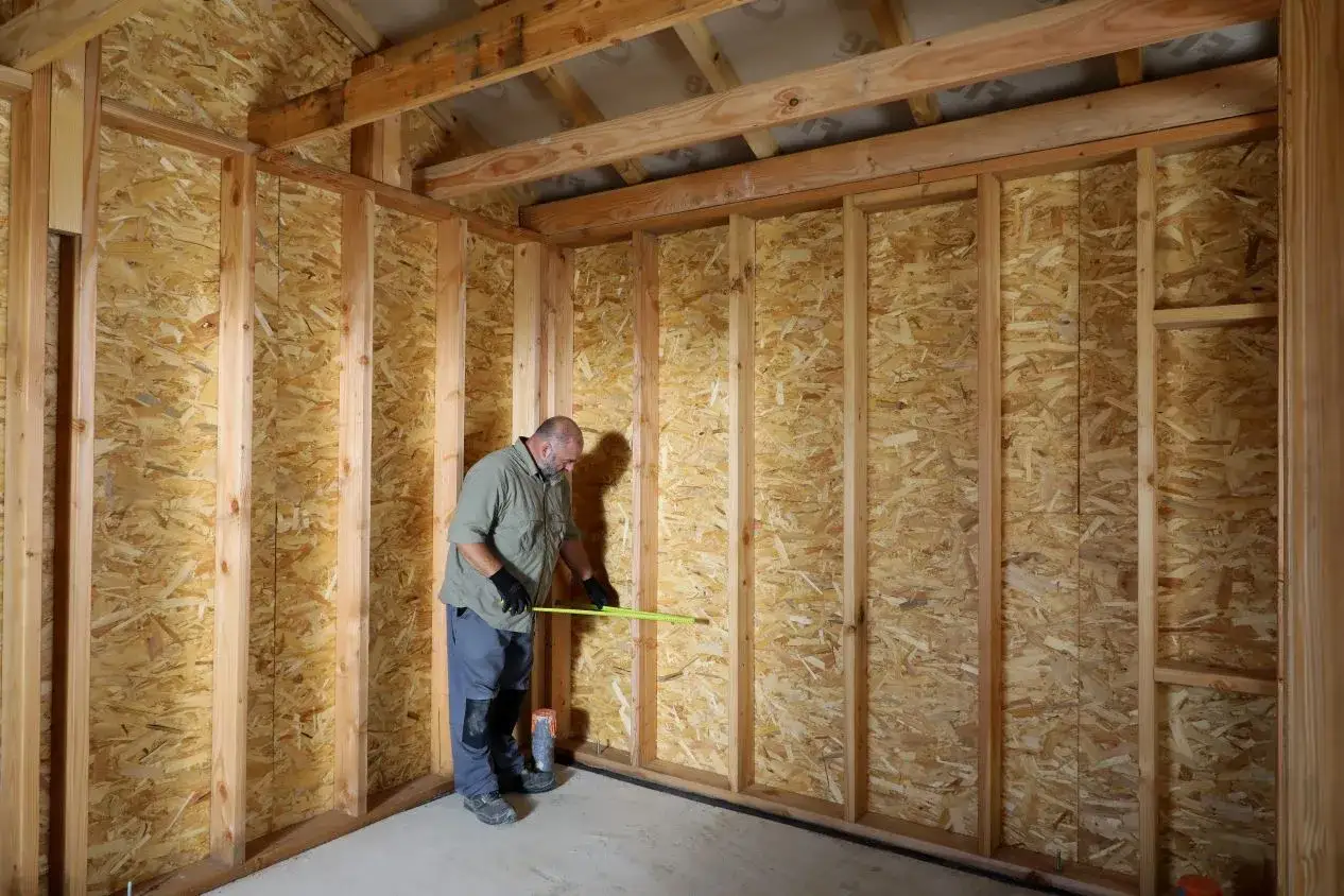 Un homme mesure un mur en panneaux OSB, soulignant la résistance thermique bois pour une construction efficace.