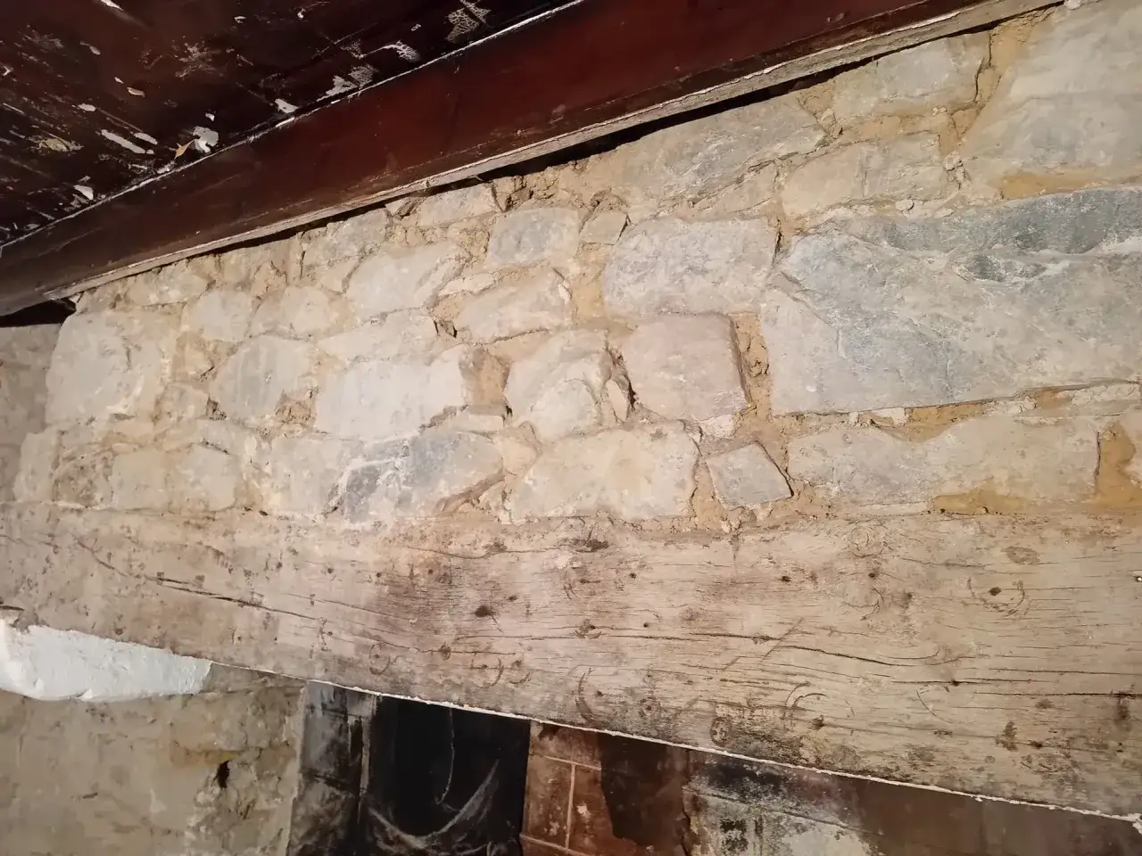 Un vieux joint mur en pierre, avec une poutre en bois patin&eacute;e par le temps, sous un plafond sombre.