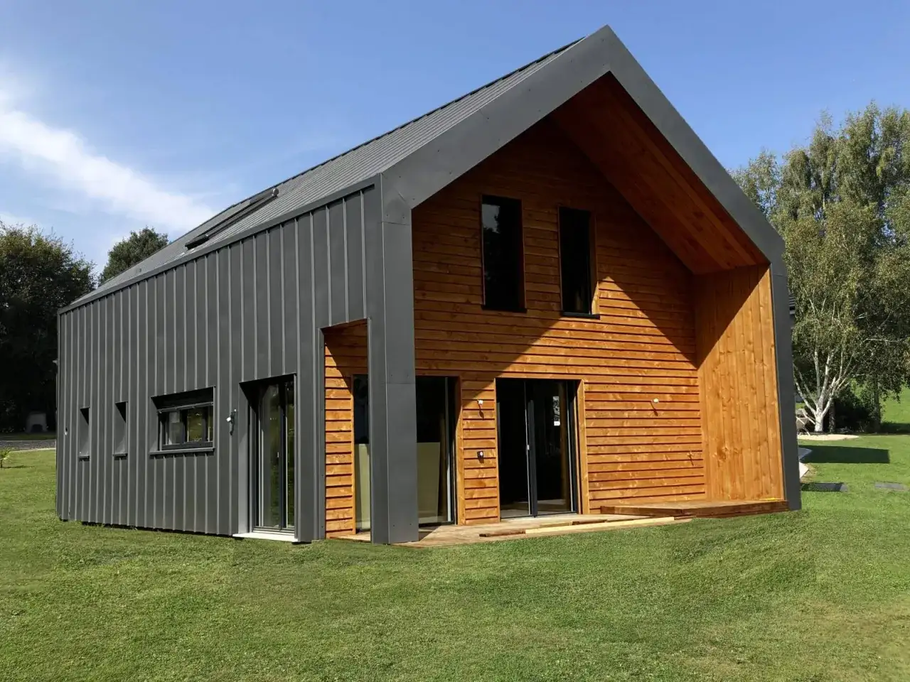 Maison moderne avec bardage en fraké bois et zinc. Le soleil éclaire la façade en bois chaleureuse.