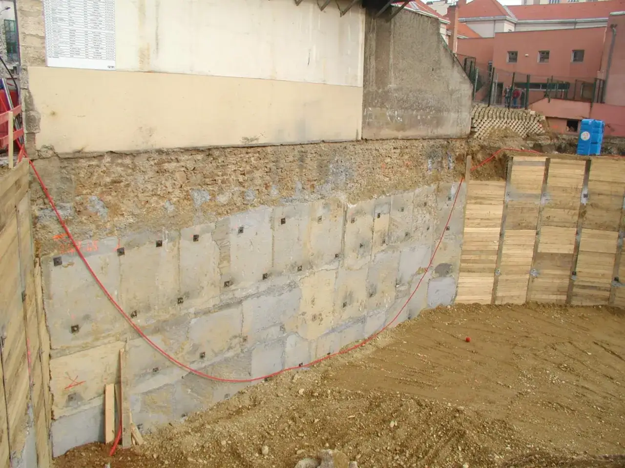 Travaux de soutènement pour la consolidation d'une fondation de maison. Murs en béton et bois, avec une ligne rouge.