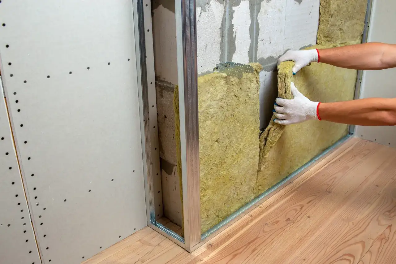 Pose d'isolant pour l'isolation phonique d'un mur de chambre. La laine de roche est insérée dans une structure métallique avant la pose des plaques de plâtre.