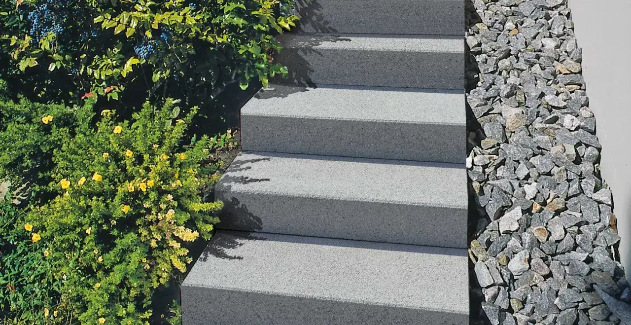 Escalier ext&eacute;rieur en b&eacute;ton gris, avec une v&eacute;g&eacute;tation luxuriante et des pierres d&eacute;coratives. La profondeur marche escalier ext&eacute;rieur est bien visible.