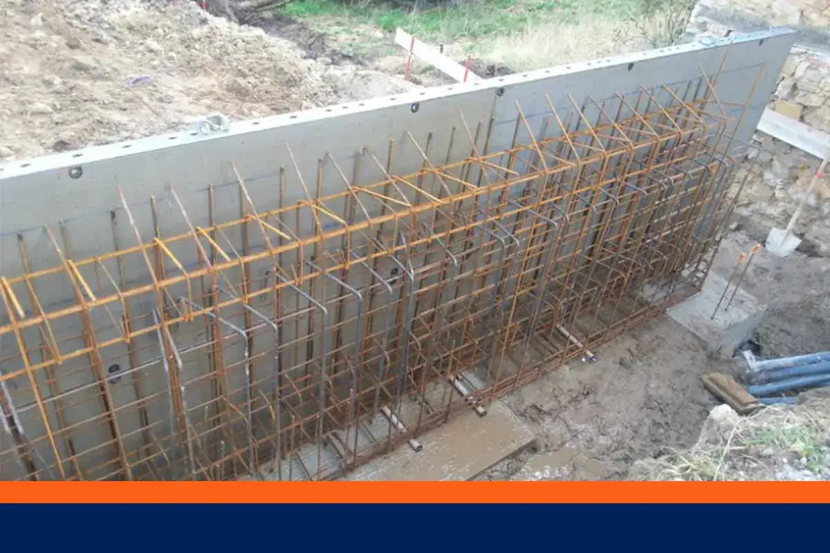 Armature en fer rouill&eacute; pr&ecirc;te &agrave; &ecirc;tre coul&eacute;e dans un mur banch&eacute;. Le chantier est en cours, la terre est meuble.