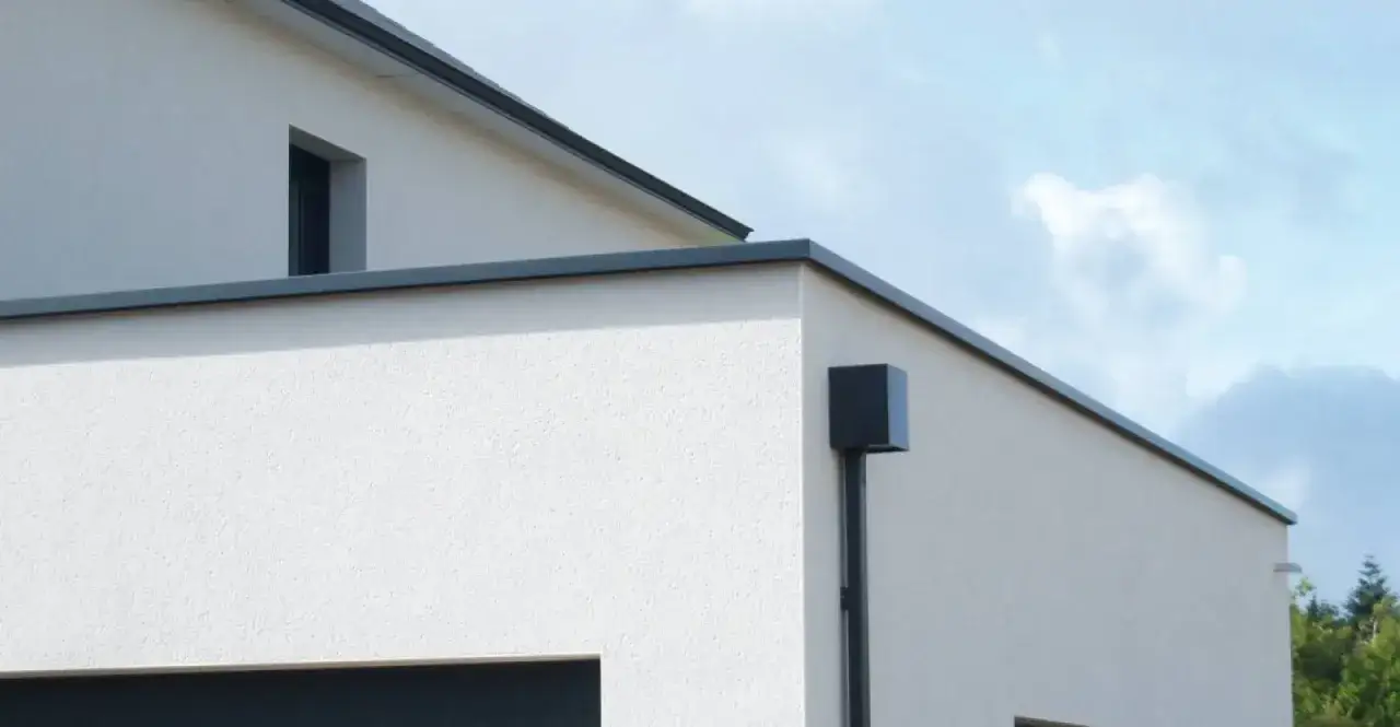 D&eacute;tail d'une maison moderne avec une goutti&egrave;re noire et sa fixation couvertine, sous un ciel bleu.