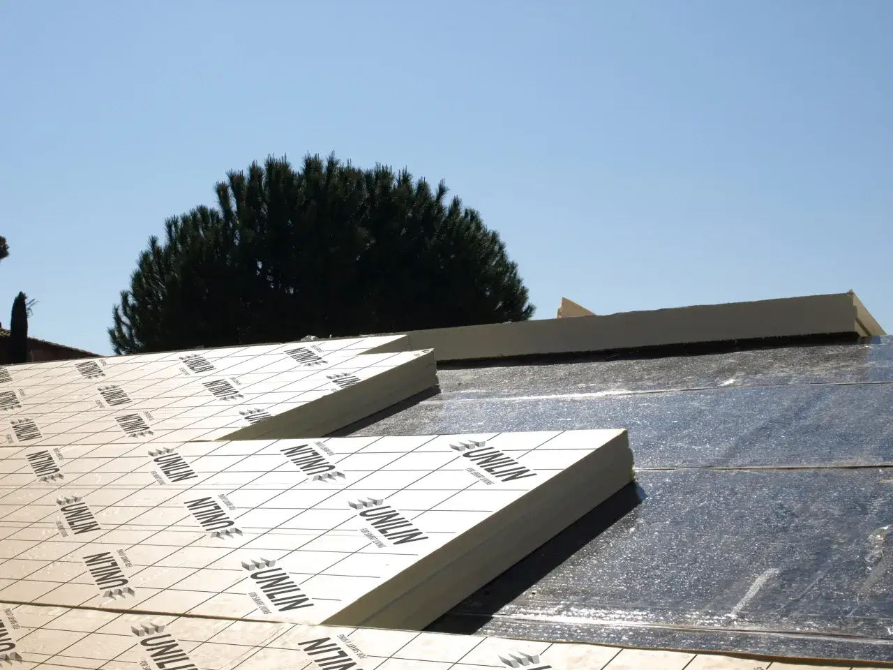 Panneaux de polyuréthane pour isolation toiture par l'extérieur. Un chantier en cours sous un ciel bleu.