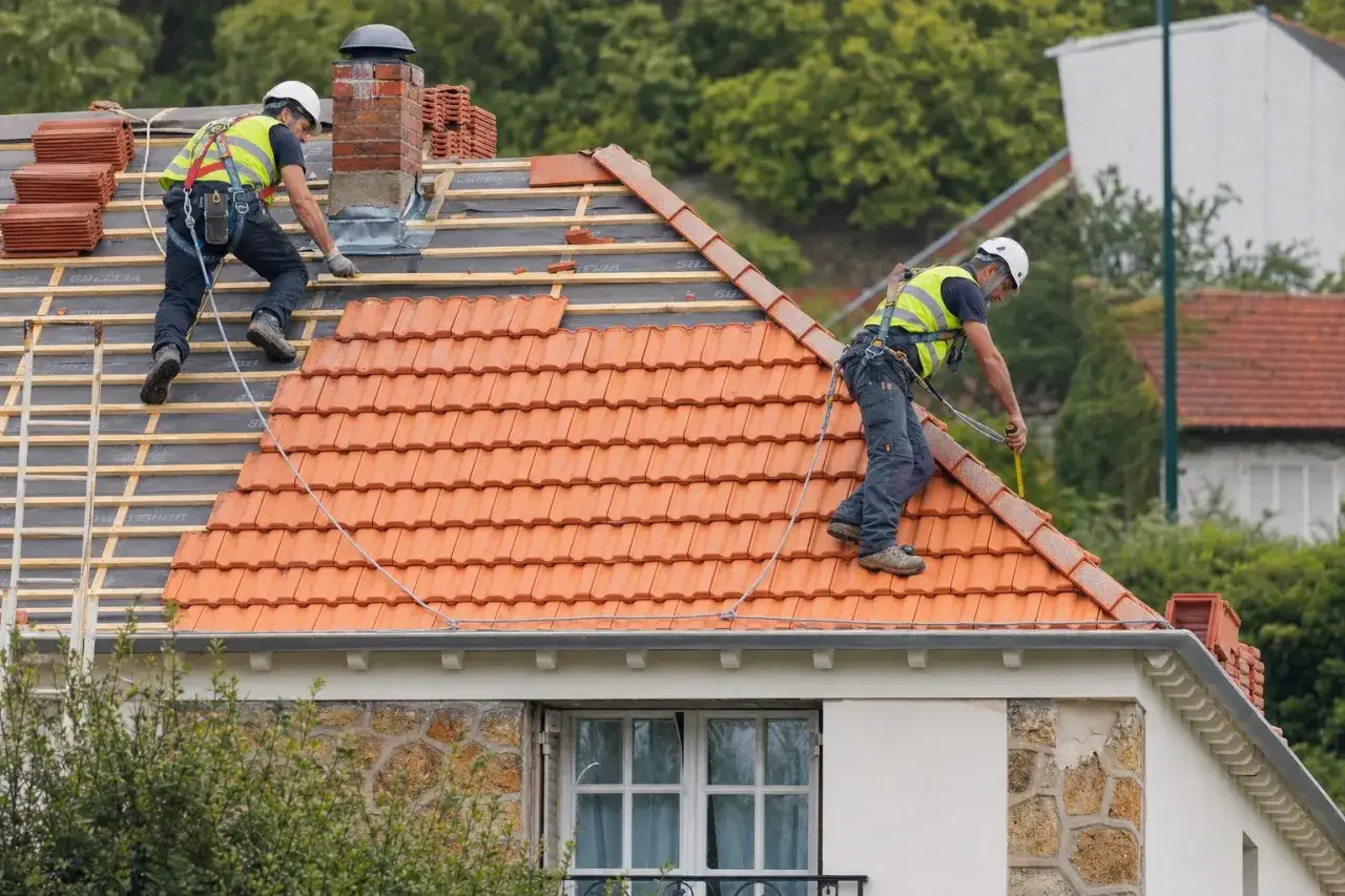 Deux couvreurs travaillent sur une r&eacute;novation toiture. L'un pose des tuiles, l'autre mesure.