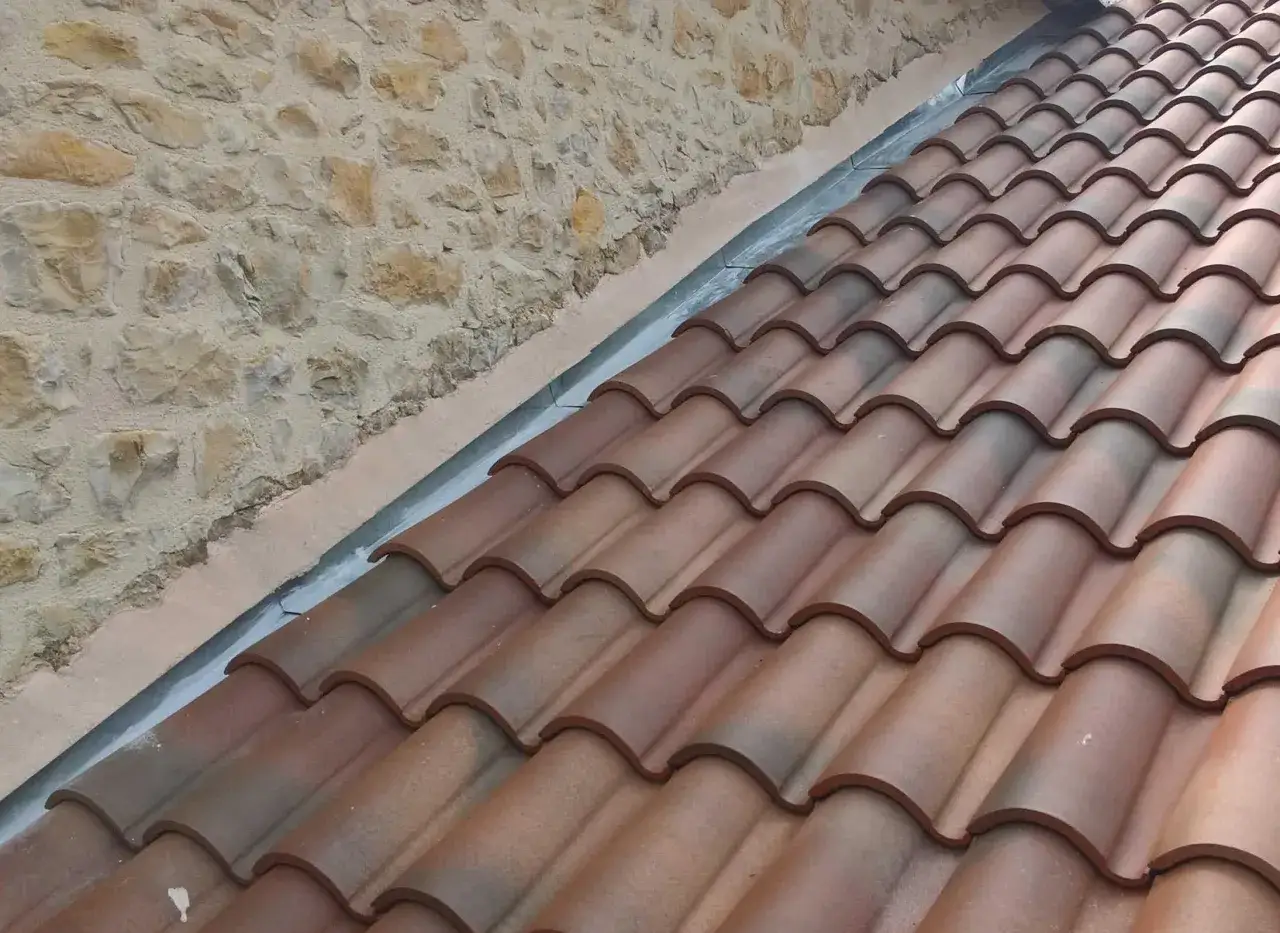 Pose d'un solin en zinc contre un mur en pierre, protégeant la jonction avec les tuiles de toiture.