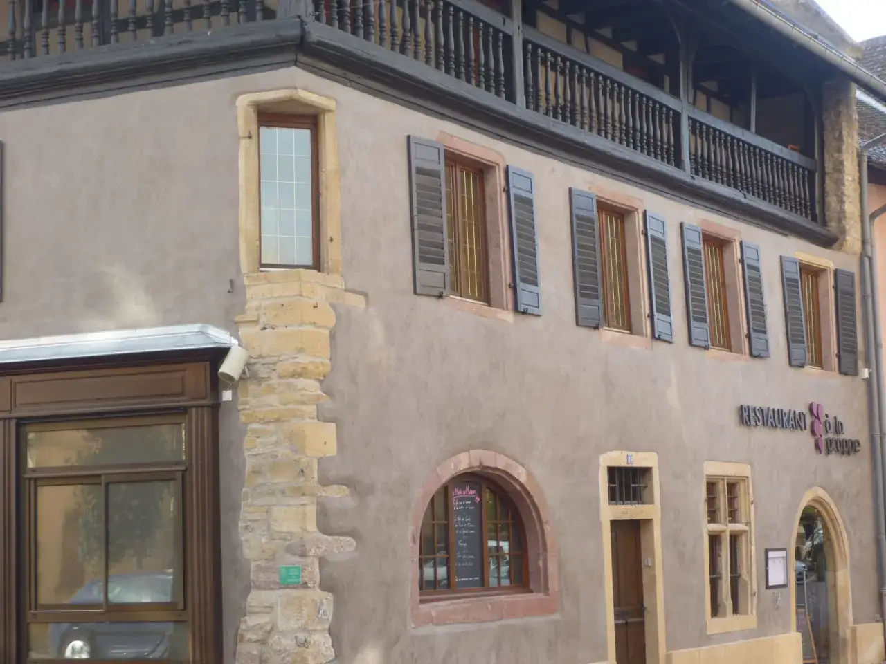 Façade d'un restaurant avec un mur à la chaux, des volets gris et un balcon en bois.