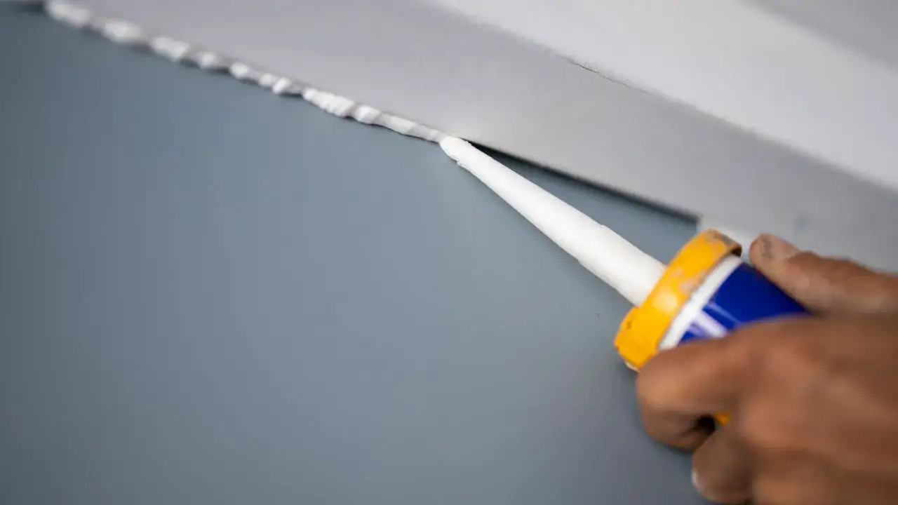 Application de mastic acrylique pour une finition parfaite. Un artisan applique le produit le long d'une plinthe.