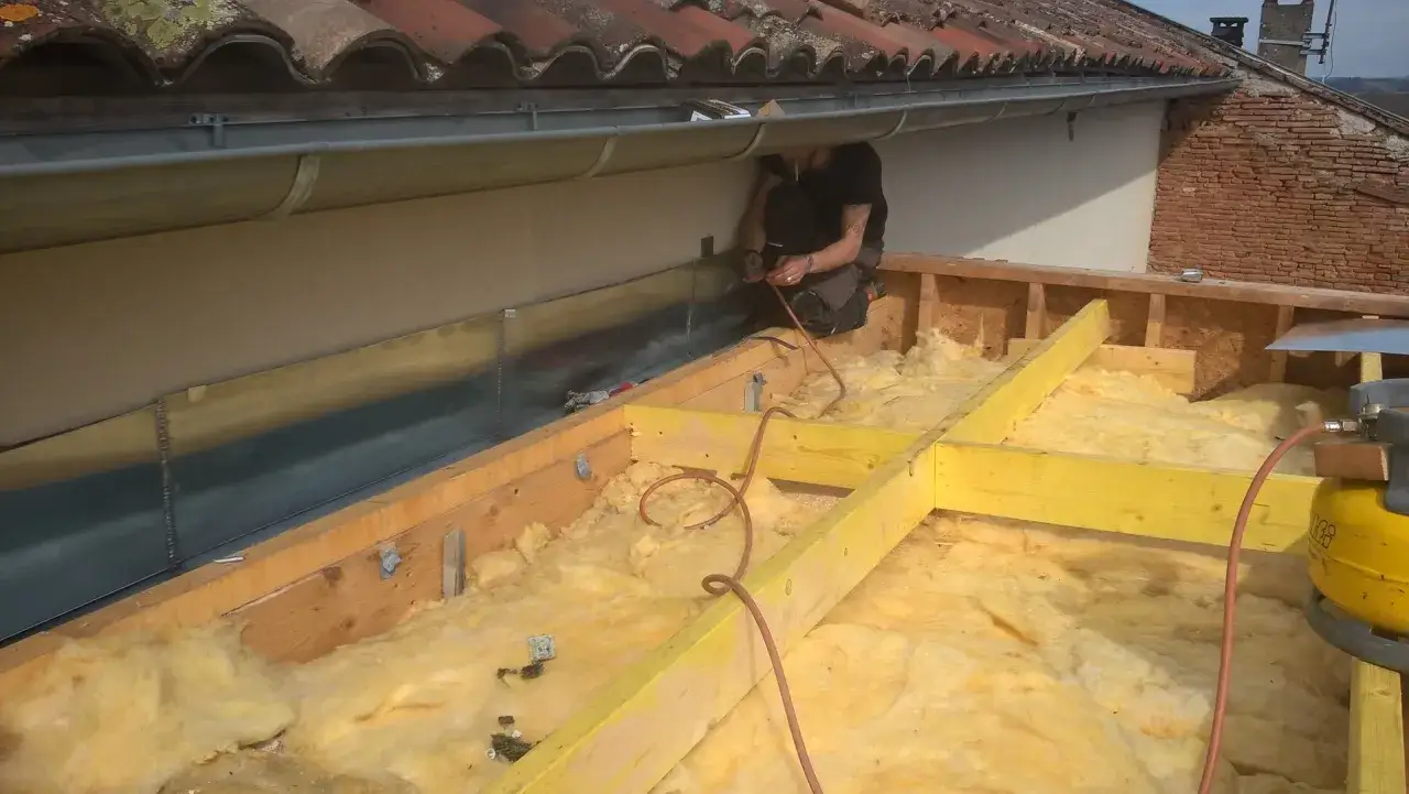 Un ouvrier installe une toiture bac acier isol&eacute;. L'isolation jaune est visible sous la structure en bois.