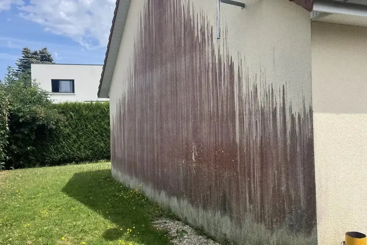 Traces sombres sur un mur extérieur, probablement dues à des algues rouges et à l'eau de javel utilisée pour le nettoyage.