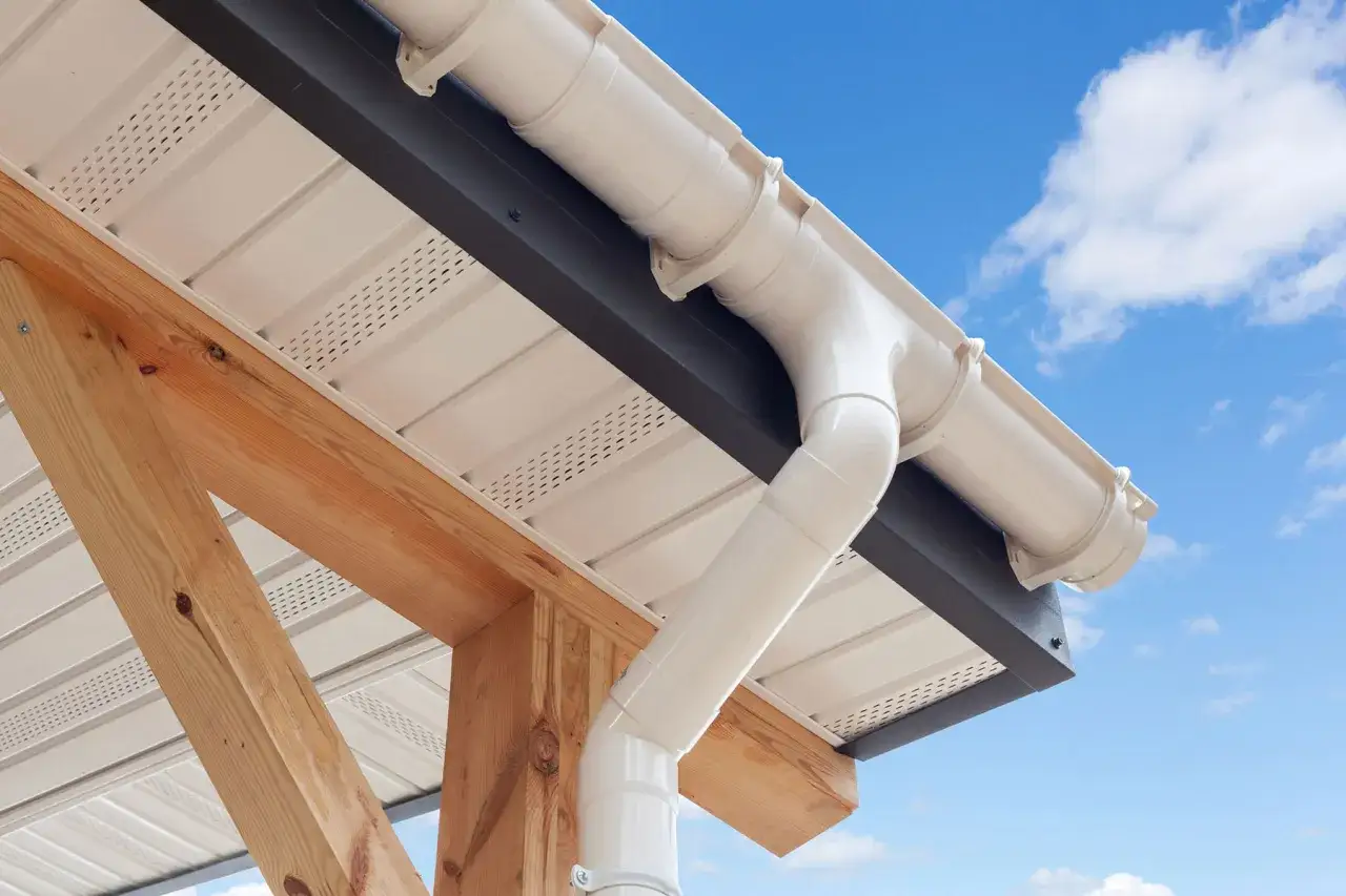 Gouttière en PVC blanc installée sur une structure en bois, avec un ciel bleu et des nuages en arrière-plan.