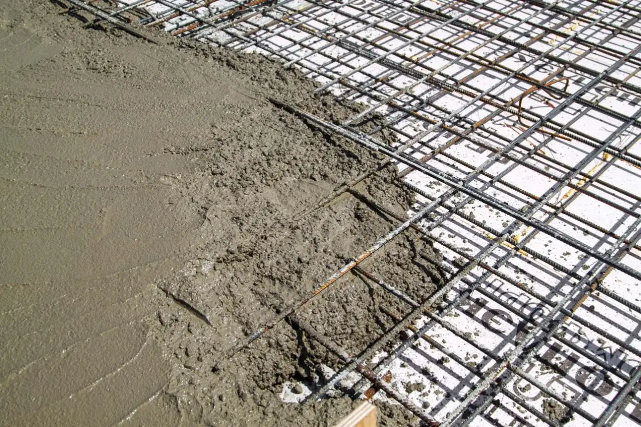 Coulée de béton frais sur une armature métallique pour la fondation d'une dalle béton. Le matériau gris est encore humide et lisse par endroits.