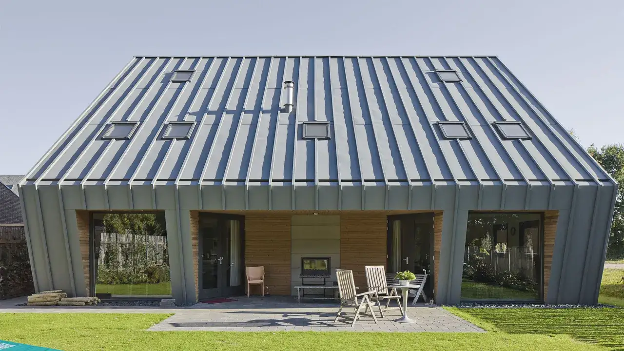 Maison moderne avec un impressionnant toit en zinc, plusieurs lucarnes et de grandes baies vitrées donnant sur un jardin verdoyant.