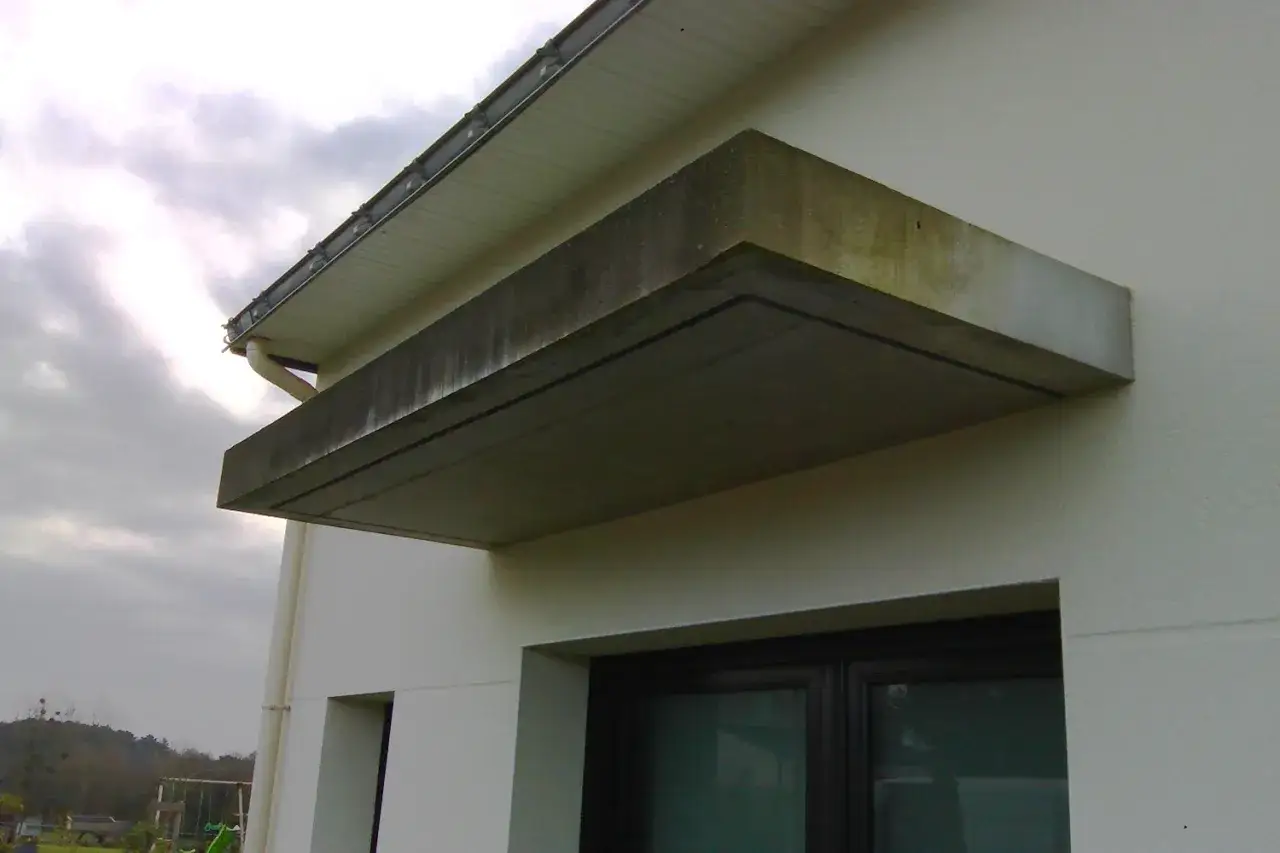 La casquette de bâtiment en béton protège une fenêtre. Le ciel est couvert.
