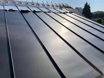 Pose de feuilles de toit en zinc sur une nouvelle construction. Le soleil brille sur le métal lisse.