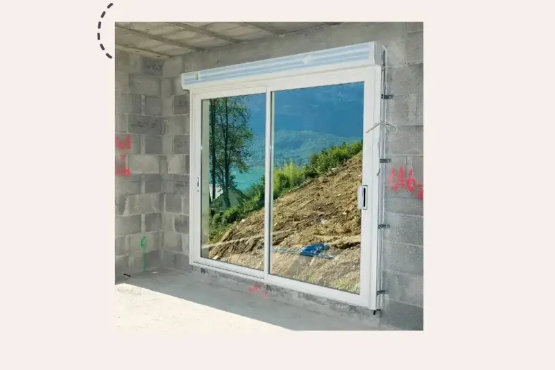 Fenêtre coulissante en PVC installée dans un mur en parpaings, offrant une vue sur un paysage montagneux. Idéal pour apprendre comment poser une fenêtre de toit.