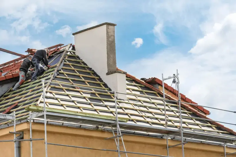 Deux couvreurs travaillent sur une toiture en cours de renovation. Des échafaudages entourent la maison.