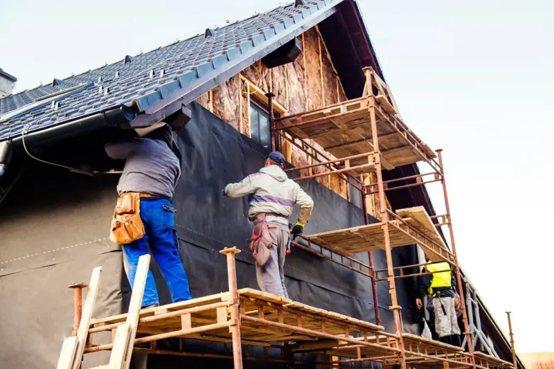 Travailleurs sur échafaudages installent une membrane pour l'isolation par l'extérieur d'une maison en construction.
